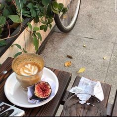 a cup of coffee sitting on top of a white plate next to a wooden table