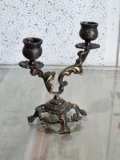 two ornate metal candlesticks sitting on top of a glass table next to a wall