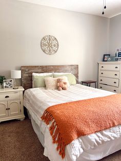 a bedroom with a bed, dressers and a teddy bear sitting on the pillow