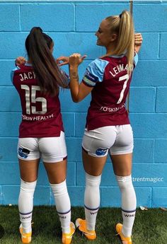 two female soccer players standing in front of a blue wall with their backs to the camera