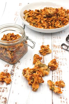 a bowl of granola next to a glass jar filled with granola flakes