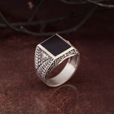 a silver ring with a black stone in the center on a brown surface next to some branches