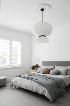 a bedroom with white walls and grey carpeting, a bed in the middle is surrounded by two round lamps