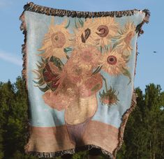 a tapestry with sunflowers in a vase hanging from a clothes line on a pole