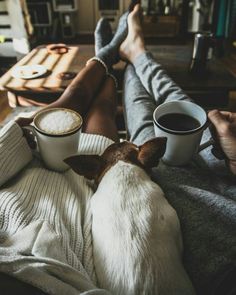 a dog sitting on top of a couch next to two people holding coffee mugs