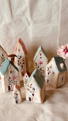 small ceramic houses with flowers on them sitting on a white cloth covered tablecloth next to a pink flower