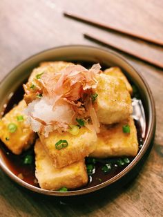 some food is in a bowl on a wooden table with chopsticks and sauce