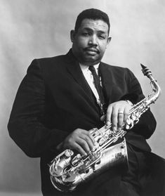 a black and white photo of a man in a suit with a saxophone on his lap