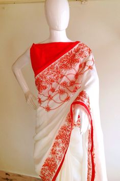 "Stunning half white semi silk saree with intricate all over embroidery and semi raw silk unstiched blouse in reddish orange. The red color thread embroidery is simply stunning aginst offwhite. The entire embroidery is hand worked and the floral border extends more in the front, pallu and the pleats. Saree length 5.5 meters Blouse fabric 1 meter 44\" wide Saree ships in 2-3 days of payment. Delivery within 4-5 days of shipment all over the world. We also offer blouse and petticoat stitching for White Silk Traditional Wear With Floral Embroidery, White Resham Embroidery Cotton Silk Blouse Piece, Red Blouse Piece With Resham Embroidery In Cotton Silk, White Cotton Silk Blouse With Resham Embroidery, Unstitched White Cotton Silk Traditional Wear, Cotton Silk Blouse Piece With Embroidered Border For Wedding, Red Traditional Wear With Floral Embroidery, Unstitched White Blouse Piece With Cutdana, Red Embroidered Cotton Silk Saree