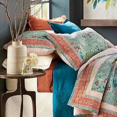 a bed with blue, orange and red comforters in a room next to a table