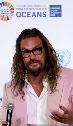 a man with long hair and glasses speaking into a microphone