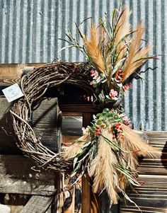 a wreath with dried flowers and leaves on top of a wooden bench next to a corrugated roof