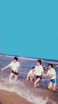 several young men are playing in the water at the beach while others watch from the shore