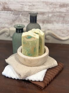 two soap bars sitting on top of a wooden bowl next to a vase and towel