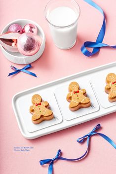 three cookies in the shape of gingerbreads on a tray next to a glass of milk