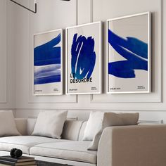 three blue and white paintings hang on the wall above a couch in a living room