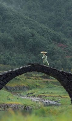 a woman walking across a stone bridge with an umbrella over her head while holding a parasol