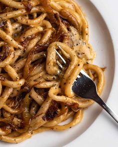 a white plate topped with pasta covered in gravy next to a silver fork