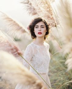 a woman standing in tall grass with her eyes closed and wearing a white dress, red lipstick