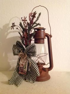 an old fashioned lantern with a bow on the handle and some plants in it sitting on a table