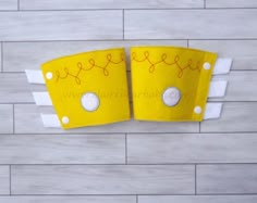 two pieces of yellow fabric with white buttons and holes in the middle on a wooden background