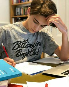 a young man sitting at a desk with his head in his hands and writing on paper