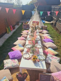 a long table is set up outside with pillows and blankets on the grass for an outdoor party