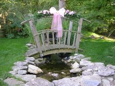 a wooden bridge over a small creek with flowers on it and a pink bow tied to the top