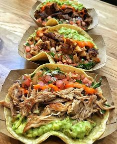 three tacos with meat and veggies on them sitting on a wooden table