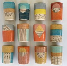 many different colored cups are lined up on a white surface, each with an abstract design