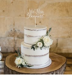 a wedding cake with white flowers and a mr and mrs sign on top is sitting on a tree stump