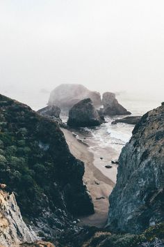 an ocean view with rocks and water in the foreground on a foggy day