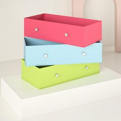 three different colored boxes sitting on top of each other in front of a white wall