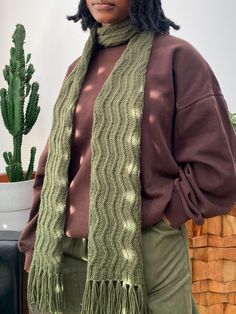 a woman standing in front of a cactus wearing a green knitted scarf and hat