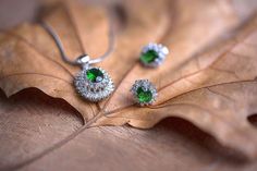 two green and white earrings sitting on top of a brown leaf next to a silver necklace