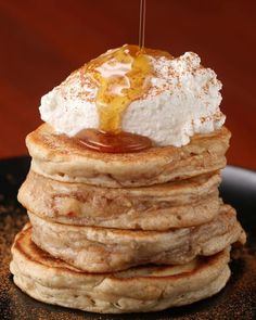 a stack of pancakes with syrup and whipped cream on top, sitting on a black plate