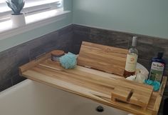 a wooden cutting board sitting on top of a bath tub next to a bottle of alcohol