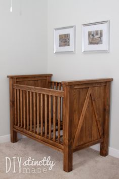 a wooden crib in the corner of a room with two pictures on the wall