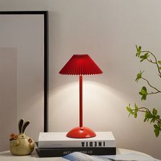 a red lamp sitting on top of a white table next to a book and potted plant