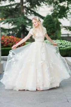 a woman in a white dress is standing on the sidewalk with her arms spread out