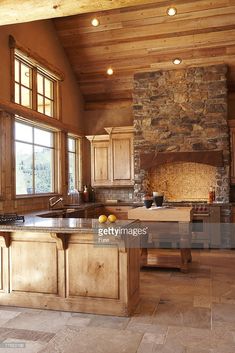 a large kitchen with an island in the middle and stone fireplace on the wall behind it