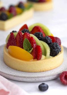 a fruit tart on a white plate with berries, kiwis and peaches