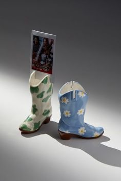 two ceramic boots are shown in front of a card holder with the image of a woman's boot on it