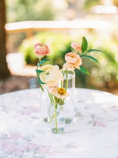 three flowers in a vase on top of a table with a floral print tablecloth