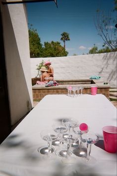 two people sitting at a table with wine glasses and cups in front of them on a sunny day