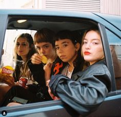 group of young people sitting in the back seat of a blue car eating and drinking