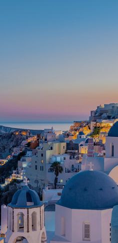 the sun is setting over some white buildings and blue domes in front of an ocean