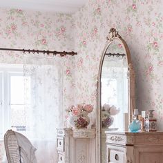 a bedroom with pink flowers on the wall and white furniture in front of a large mirror