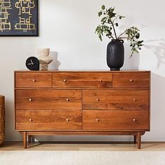 a wooden dresser with two vases on top of it next to a potted plant