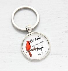 a red bird sitting on top of a metal keychain that says, cardinals appear when angels are near